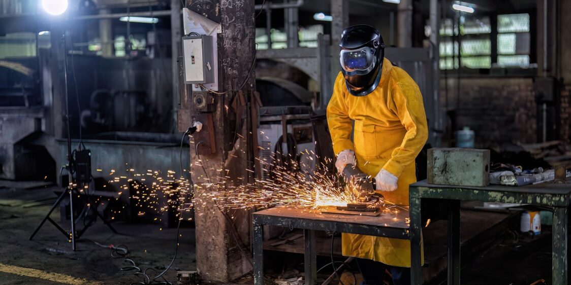Maintenance mechanical man wearing leather body protection use grinding machine cutting fire spark A worker at a contract manufacturing company cuts a piece of metal for a job.