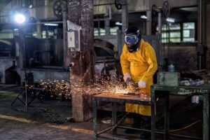 A worker at a contract manufacturing company cuts a piece of metal for a job.