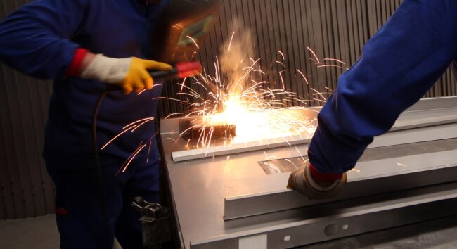 Two mature men working as welders in a metal fabrication factory. Two mature men working on component manufacturing in a metal fabrication factory.