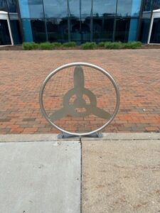 A custom welded metal installation paver guard with an interior propeller design sits in front of a brick sidewalk with a building behind.