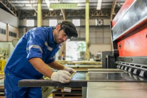 Male industrial worker measures a piece of sheet metal in a manufacturing plant.