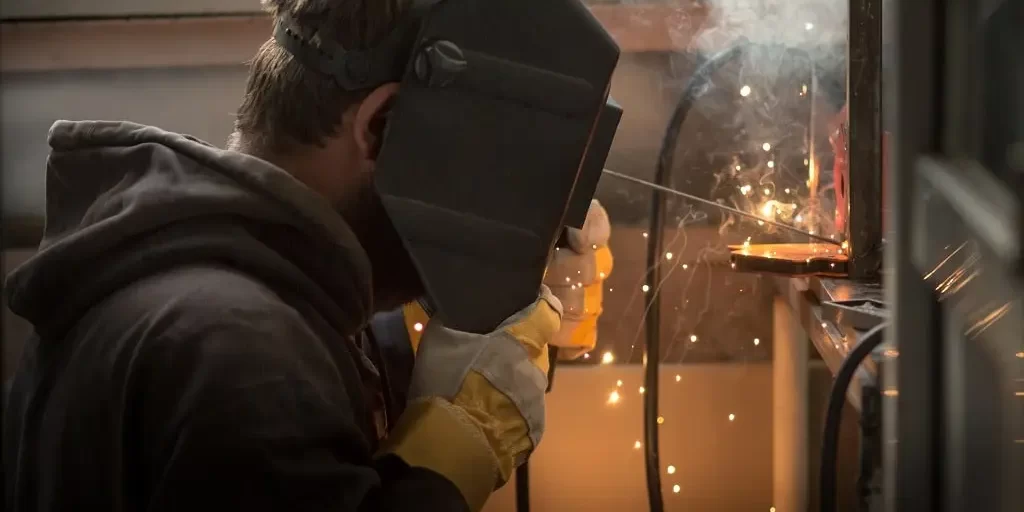 a-man-with-a-welding-machine-welds-a-metal-structu-2023-11-27-05-22-16-utc-min A young man with a welding mask and tool performs welding repairs on a metal structure.