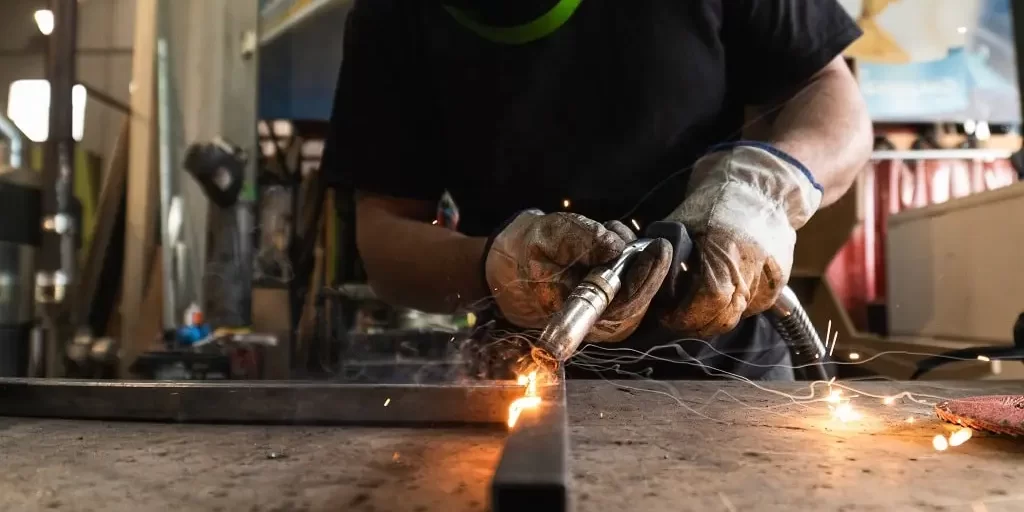 welder-in-protective-helmet-welding-metal-detail-i-2024-05-11-02-14-30-utc-min A welder in a protective helmet welds together two metal bars.