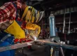 Skilled worker in protective gear performs metal fabrication by welding two metal rods together.
