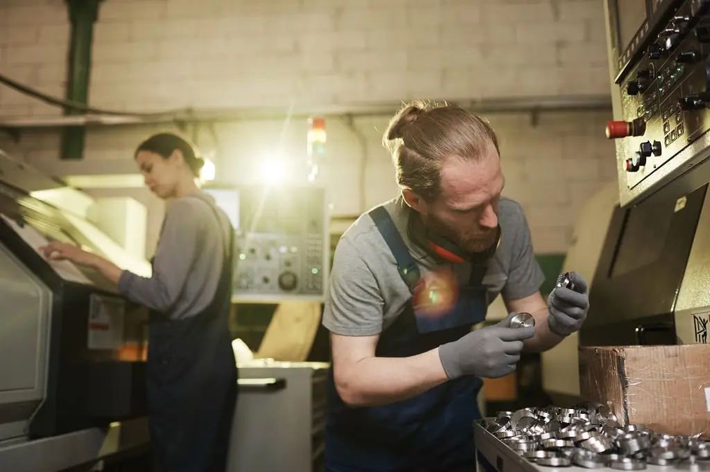 A man and woman produce small metal component parts in a metal manufacturing plant.