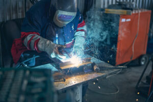 Concentrated repairman bowing his head while looking at sparks from protecting mask