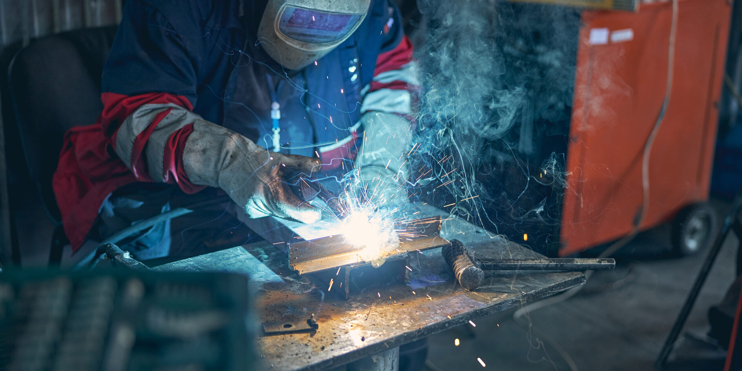 Concentrated repairman bowing his head while looking at sparks from protecting mask