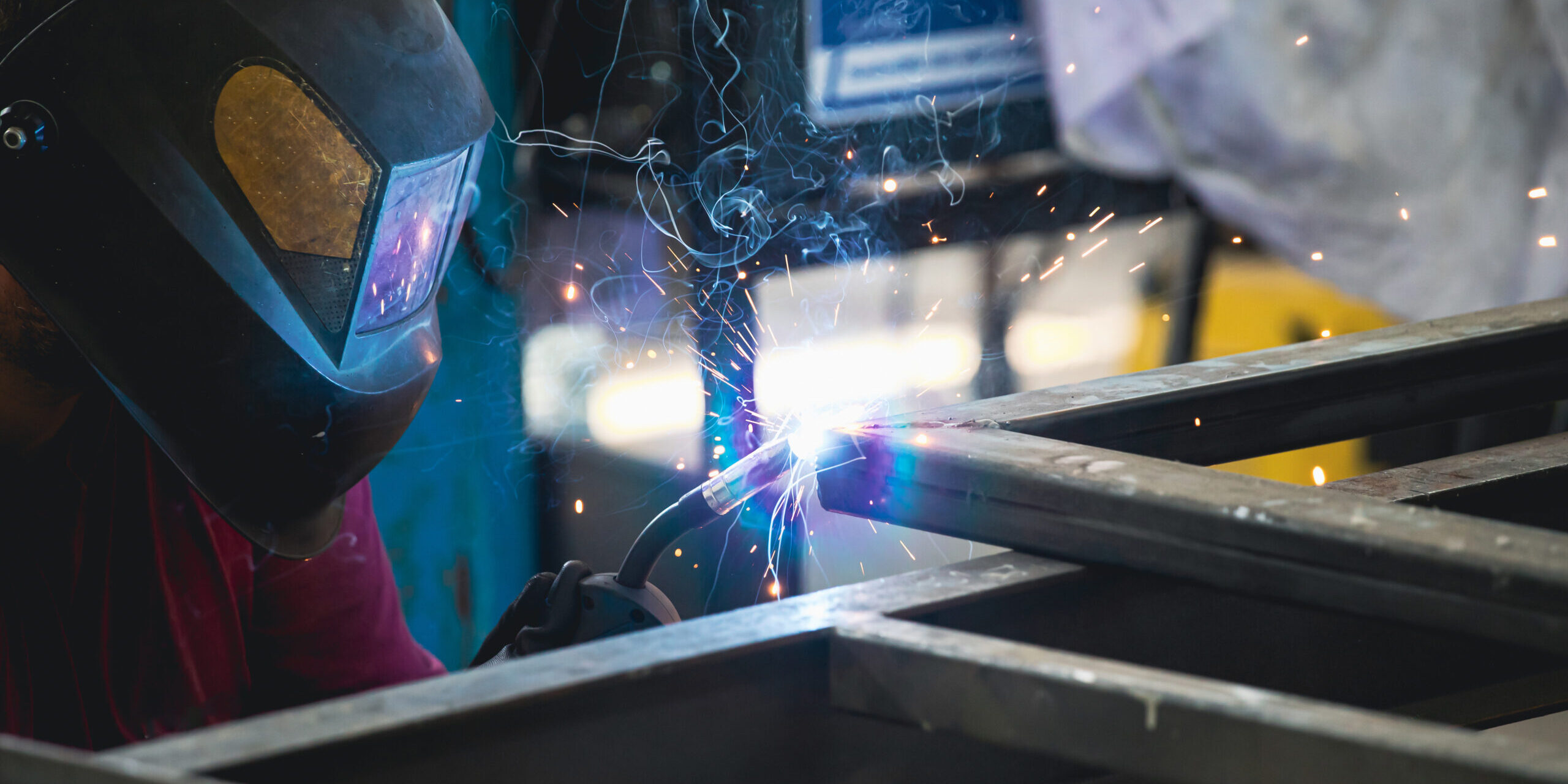 Handyman performing welding and grinding at his workplace in the workshop, while the sparks "fly" all around him. He is wearing a protective helmet and equipment.