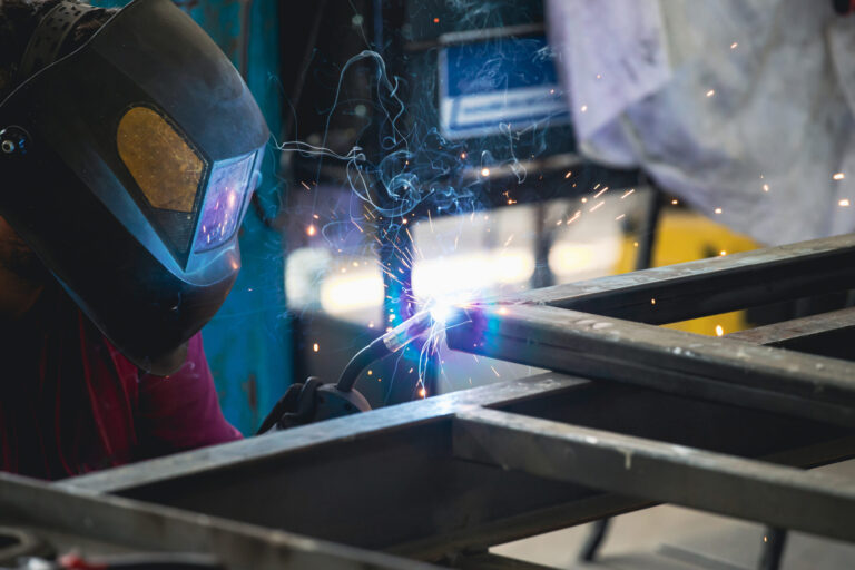 Handyman performing welding and grinding at his workplace in the workshop, while the sparks "fly" all around him. He is wearing a protective helmet and equipment.